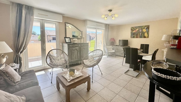 A living room with a sofa, two chairs, a small table, a TV, a painting, and a balcony with a view.