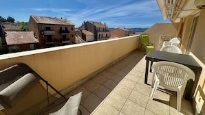 A balcony with a table and chairs, a view of buildings, and a clear sky.