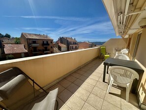 A balcony with a table and chairs, a view of buildings, and a clear sky.