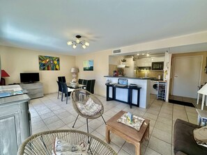 A living room with a TV, dining area, kitchen, and a ceiling fan.