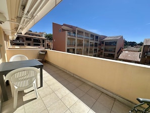 A balcony with a table and chairs, overlooking a residential area with multi-story buildings.