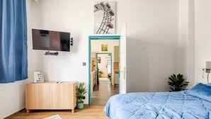 Een slaapkamer met een groot bed, een aan de muur bevestigde televisie, een houten kast en een bloempot met plant.