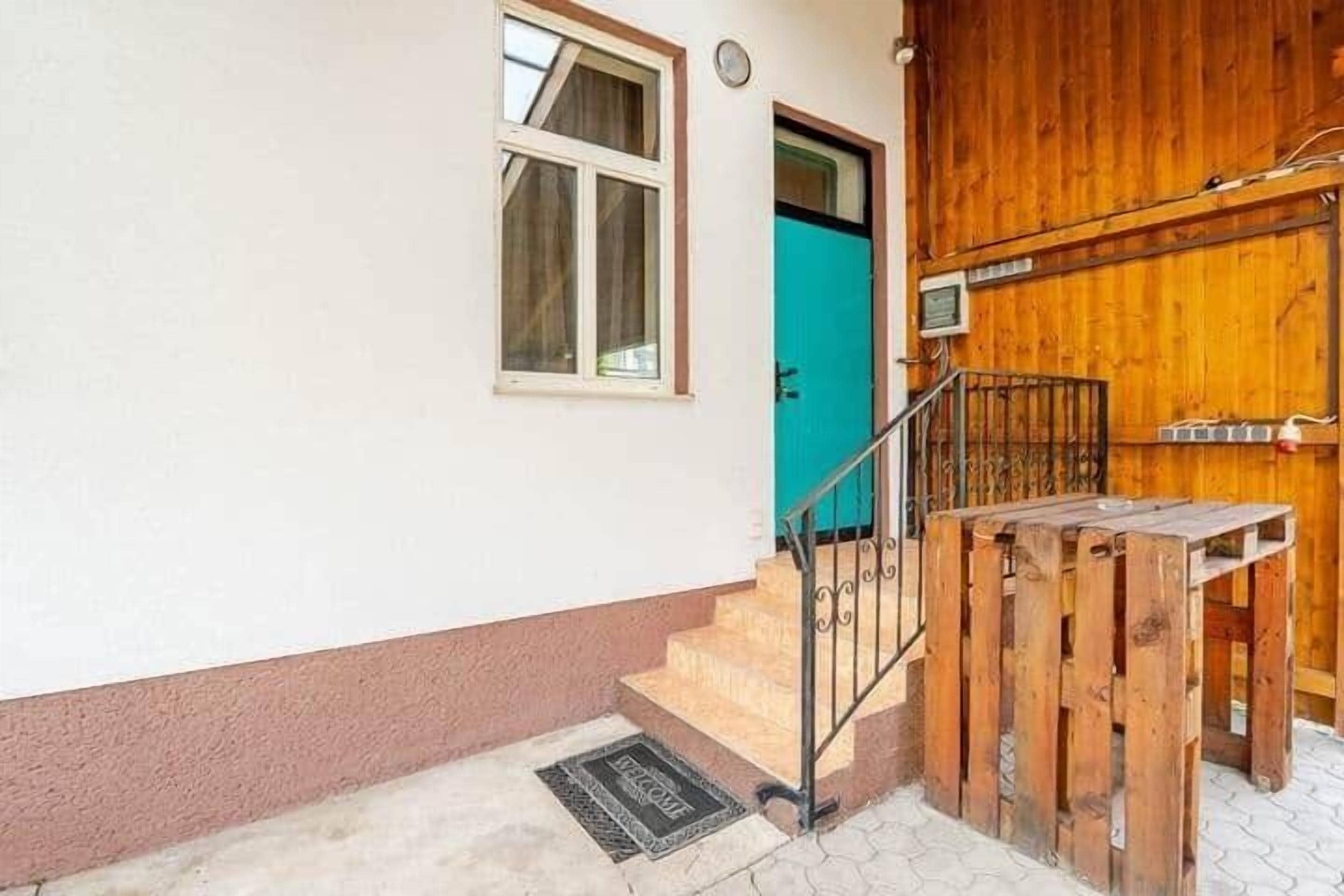 Uma escadaria que leva a uma porta de madeira, uma pequena janela e um corrimão de metal.