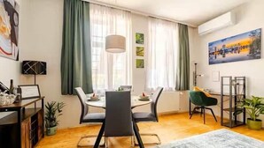 Een moderne eetruimte met een houten vloer, een ronde tafel met vier stoelen en een groot raam met groene gordijnen.
