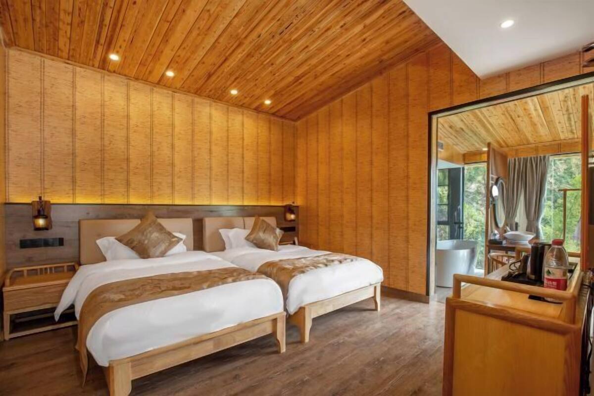 A wooden-paneled room with two beds, a wooden bench, and a large window.