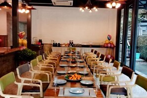 Una larga mesa de comedor con sillas, dispuesta para una comida, en una habitación con ventanas grandes y vistas al exterior.