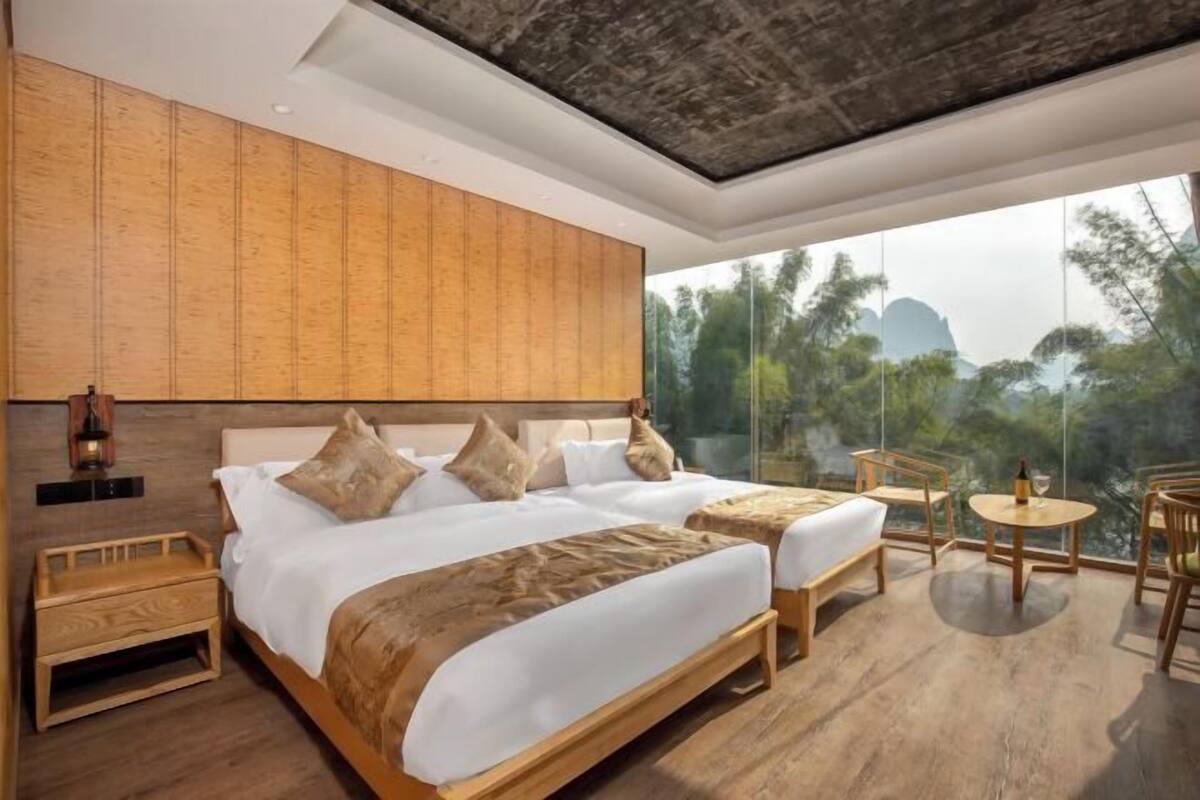 A modern hotel room with a large bed, two smaller beds, a balcony with a view, and a wooden floor.