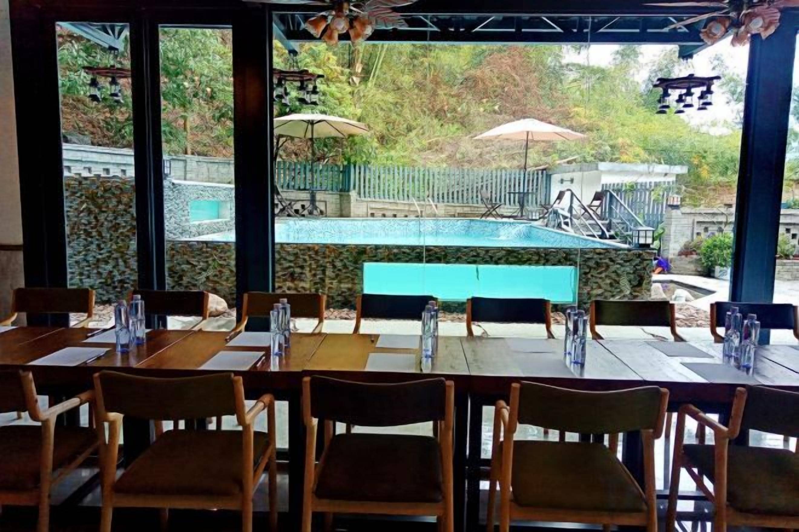 An outdoor dining area with tables and chairs, a pool in the background, and umbrellas.