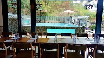 An outdoor dining area with tables and chairs, a pool in the background, and umbrellas.