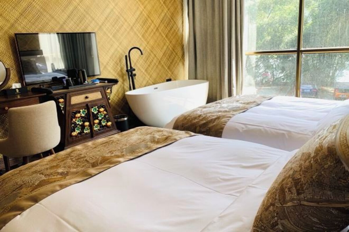 A hotel room with two beds, a TV, a desk, and a bathtub.
