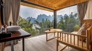 Una habitación con techo de madera, un ventanal con vistas a montañas, una mesa con un cuenco y una botella de vino, y un sofá con cojines.