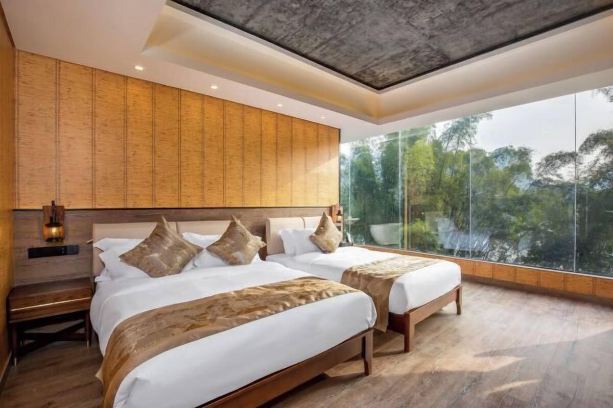 A modern hotel room with two beds, a large window with a view of trees, and a wooden ceiling.