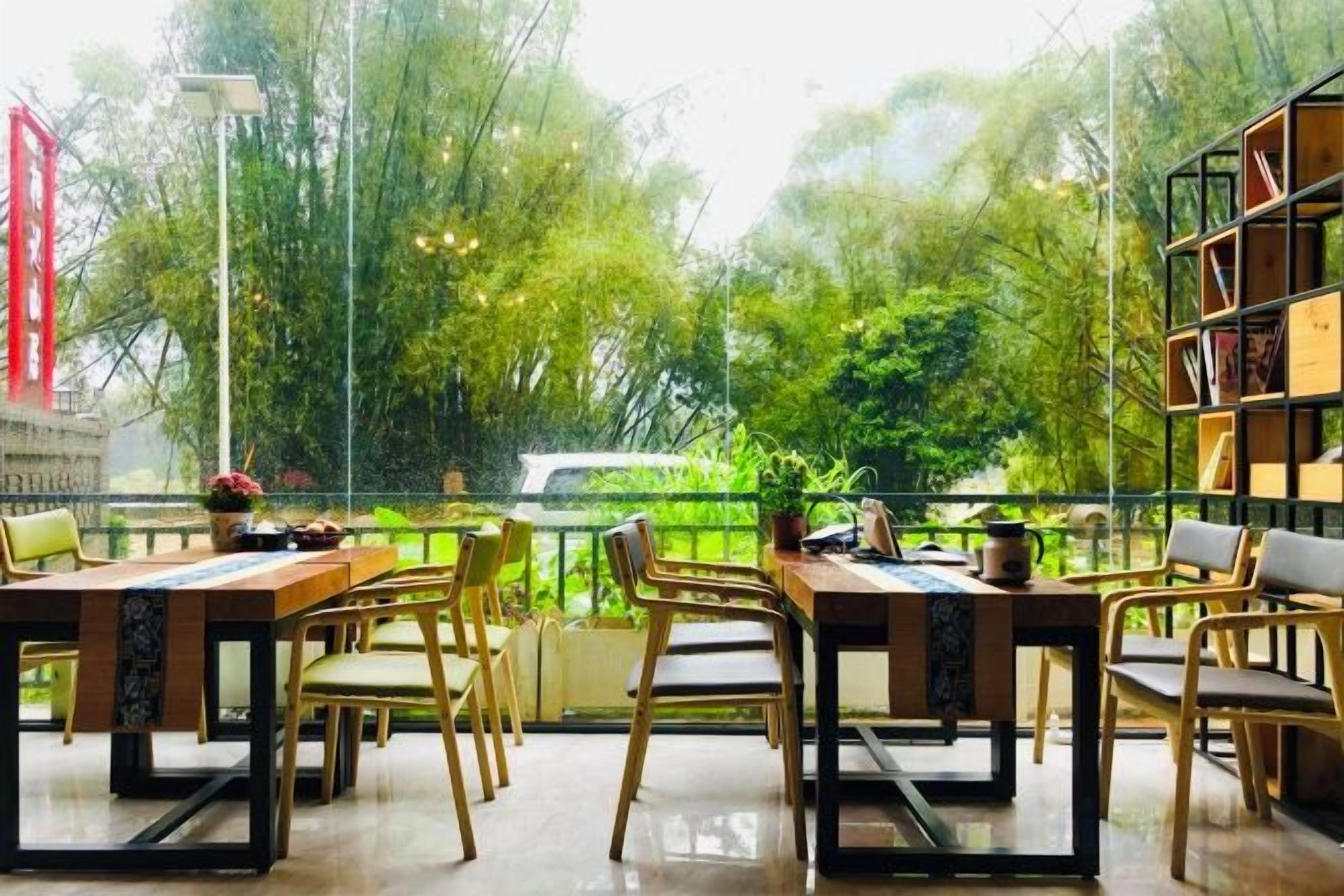 An outdoor dining area with tables and chairs, surrounded by greenery and a view of trees.