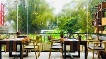 An outdoor dining area with tables and chairs, surrounded by greenery and a view of trees.