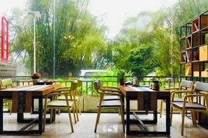 Un espacio de comedor al aire libre con mesas y sillas, rodeado de follaje y vistas a árboles.
