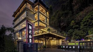 Un hotel moderno de varios pisos con fachadas de vidrio, un área de estar al aire libre cubierta y montañas al fondo.