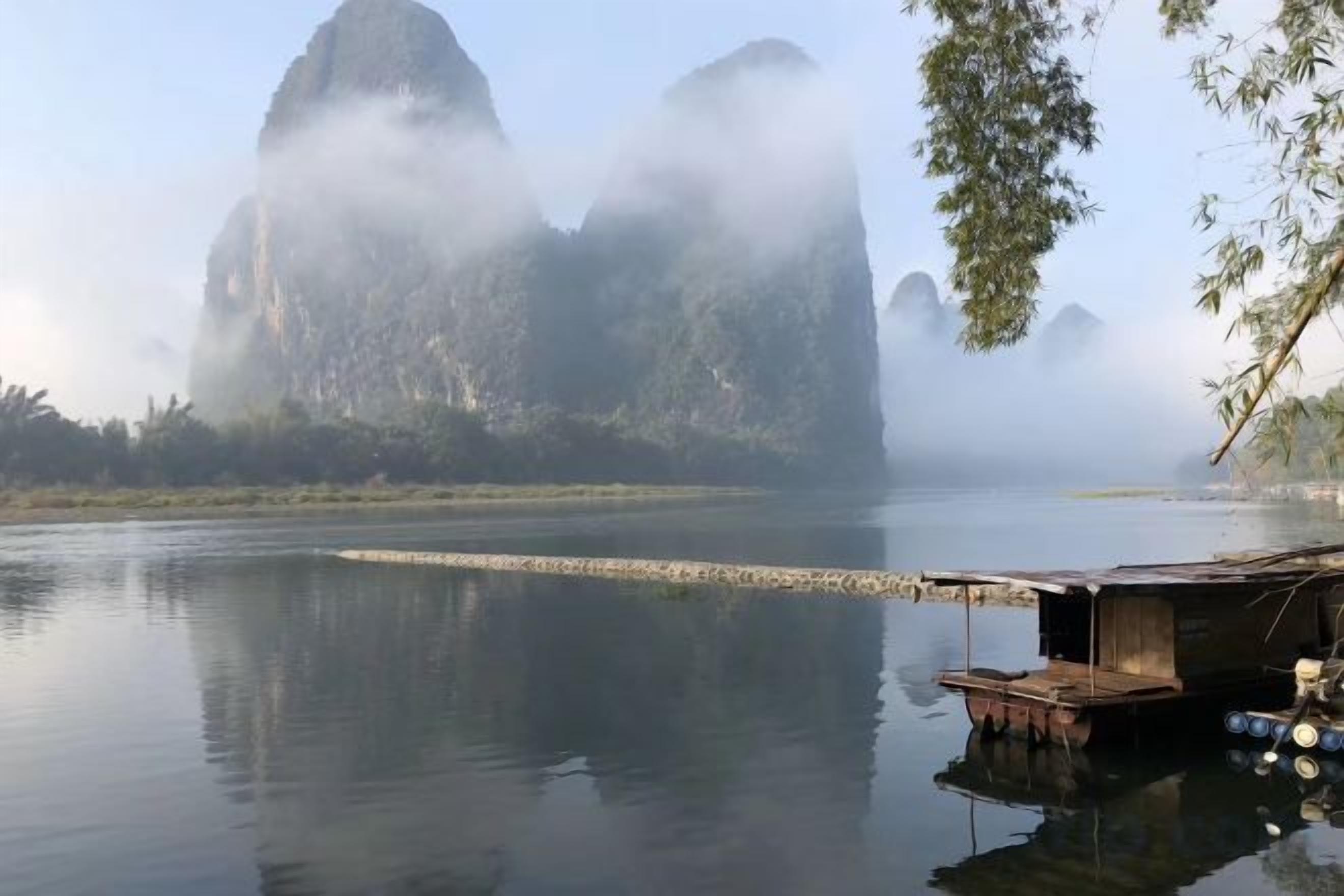 A calm river with a floating structure, surrounded by mist-covered mountains.