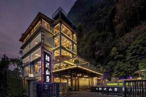 Un hotel de varios pisos con fachada de vidrio, zona de estar al aire libre y señalización que indica el nombre.