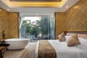 Camera d'albergo moderna con un letto grande, una vasca da bagno e vista sugli alberi tramite una porta in vetro.