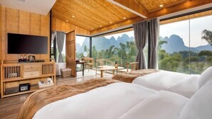 Una habitación de hotel moderna con una cama grande, techo de madera, televisor, escritorio y una vista panorámica a las montañas.
