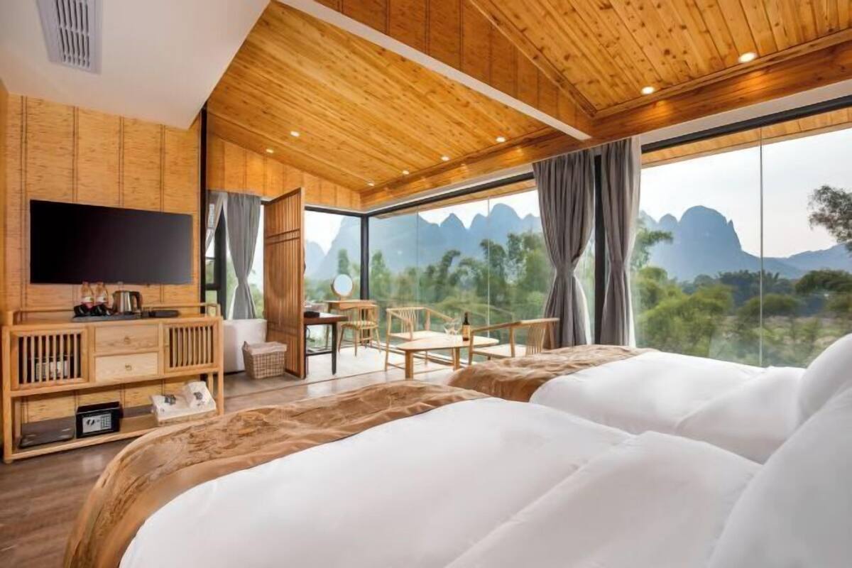 A modern hotel room with a large bed, wooden ceiling, a TV, a desk, and a scenic mountain view.
