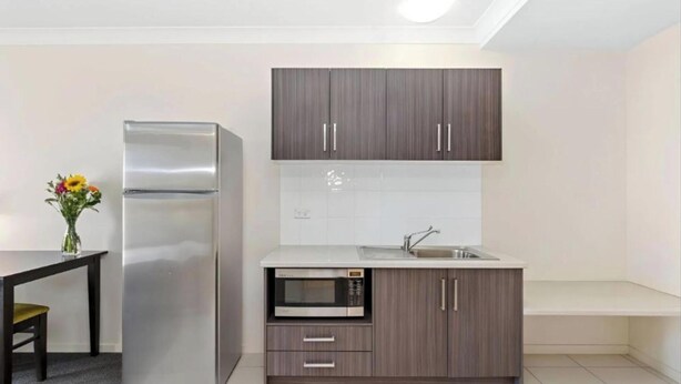 A compact kitchen with a refrigerator, microwave, and wooden cabinets.