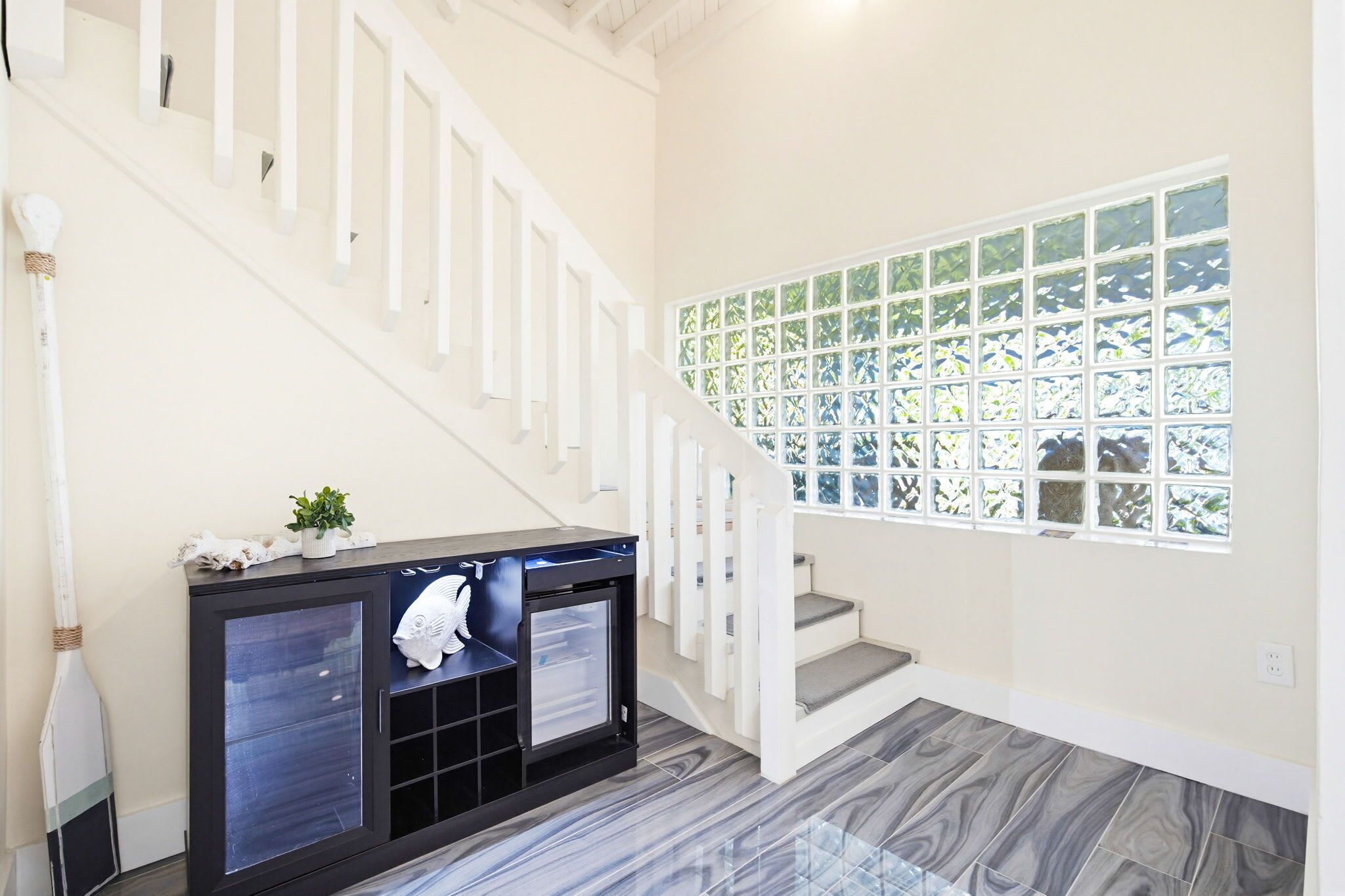 A staircase with white railings, a black console table with a plant, and a window with a green leafy pattern.