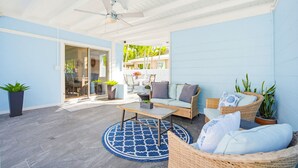 Une terrasse couverte avec un ventilateur de plafond, des meubles en osier, un tapis rond et des plantes en pot.