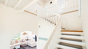 Un intérieur moderne avec un escalier, un espace de vie comprenant un canapé et une table basse, et une pancarte indiquant « BIENVENUE ».