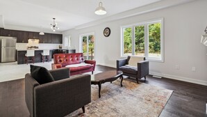 Amplia sala de estar con una cocina moderna, un sofá de cuero rojo, un sillón gris y un ventanal con vistas al exterior.