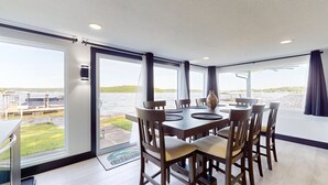 A dining area with a table and chairs, large windows with a view of a body of water and dock, and a door leading outside. - Grandview Luxe Retreat - Gravois Arm (Gravois Mills)