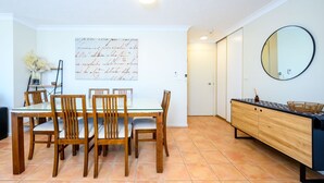 A dining area with a white table and wooden chairs, a large framed artwork on the wall, and a wooden cabinet with a mirror.