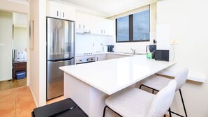 A modern kitchen with white cabinetry, a stainless steel refrigerator, a large island with bar stools, and a window above the sink.