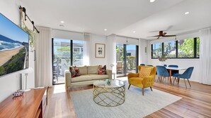 A spacious living area with a large window, a sofa, a coffee table, and a dining area with chairs.