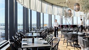 A modern restaurant with high ceilings, large windows, and a view of the city.