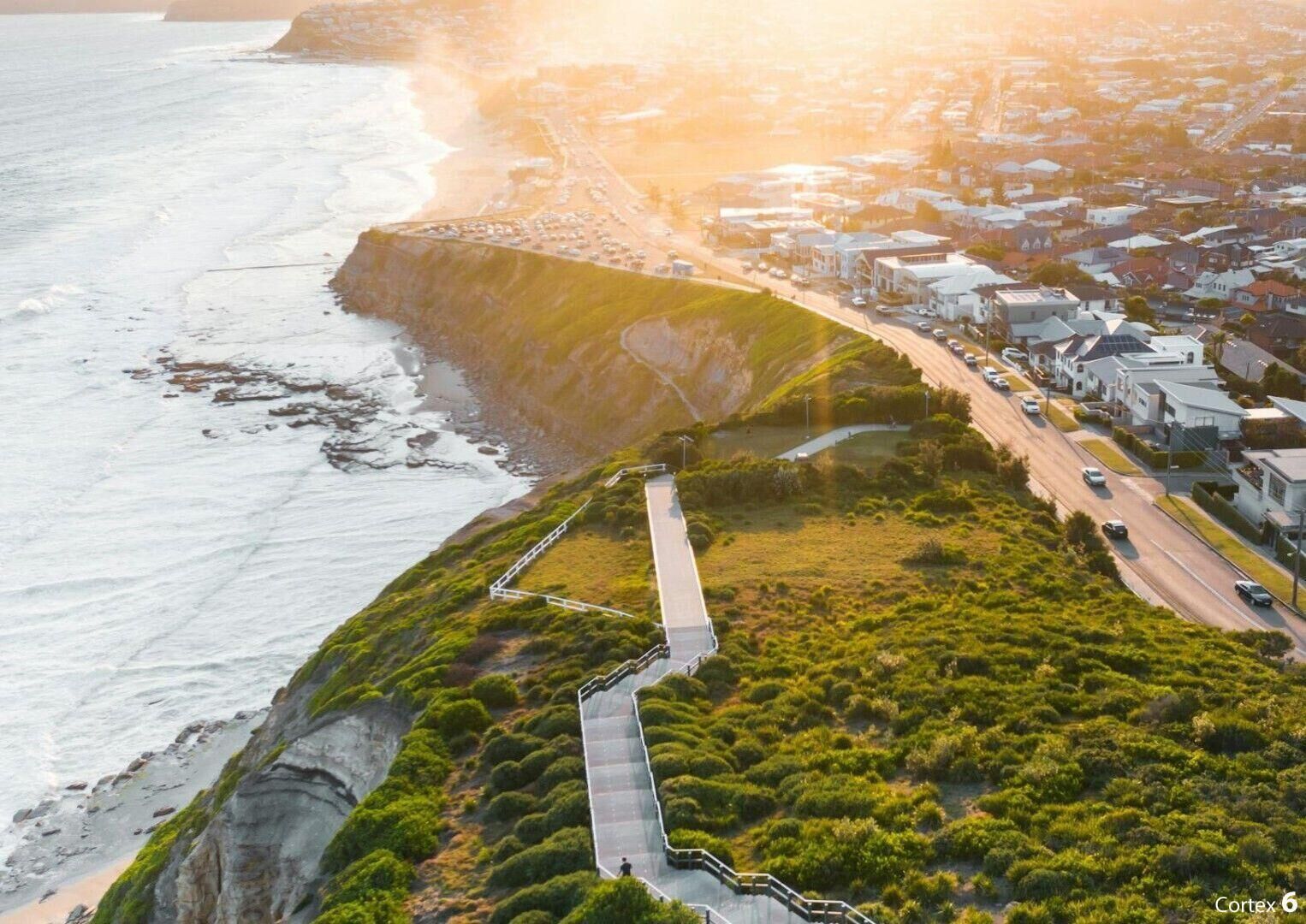 Vue aérienne d’une ville côtière, avec une falaise imposante, une route menant à une plage et des immeubles d’habitation.