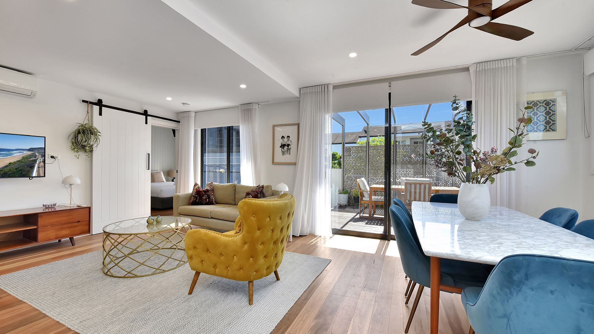 A modern living room with a sofa, yellow armchair, and a dining area with a table and chairs.