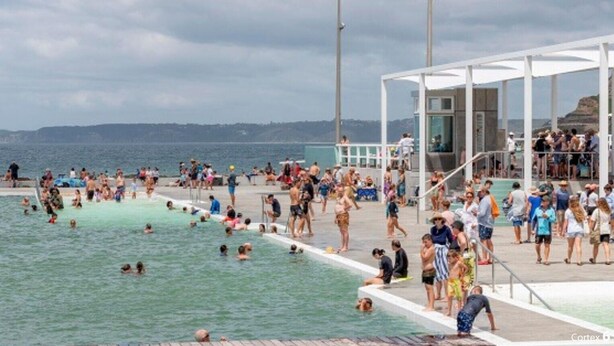 A crowded outdoor swimming pool with people enjoying the water and sunbathing.