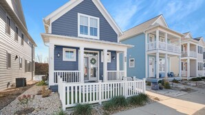 A two-story residential building with a front porch, a visible door, and a small garden area with gravel and plants.