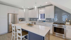 A modern kitchen with white cabinetry, a marble island, stainless steel appliances, and a blue accent wall.