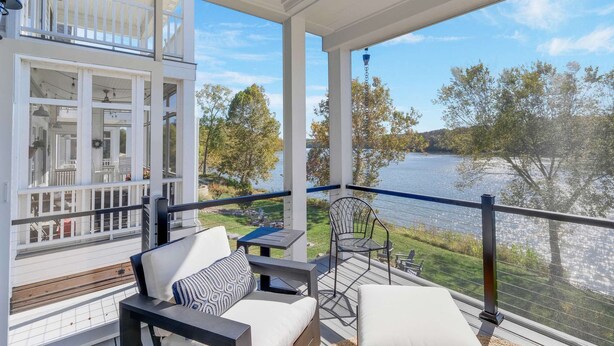 A balcony with outdoor furniture, a view of a lake, and a building with multiple windows.