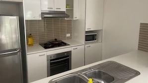 A kitchen with white cabinets, a stainless steel refrigerator, a microwave, and a sink. - Nice (Kuraby)