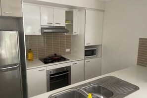 Eine Küche mit weißen Schränken, einem Edelstahl-Kühlschrank, einer Mikrowelle und einem Spülbecken.