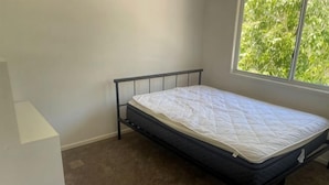 A single bed in a room with a window, carpeted floor, and white walls. - Nice (Kuraby)