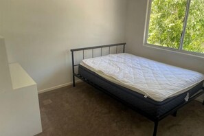 Ein Einzelbett in einem Zimmer mit Fenster, Teppichboden und weißen Wänden.