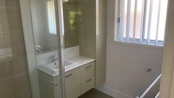 A bathroom with a glass shower enclosure, a white sink, and a window with vertical blinds.