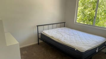A single bed with a metal frame and a white mattress in a room with a window.