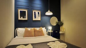 Ein ordentlich bezogenes Bett mit Kissen, ein Nachttisch mit Lampe, ein wandmontierter Spiegel und gerahmte Kunstwerke.