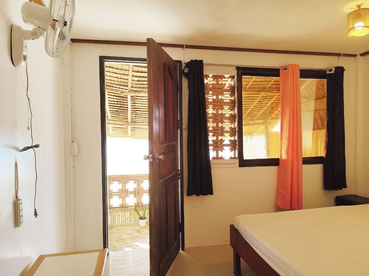 A room with a bed, a fan, a door, and a window with curtains.