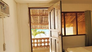 Quarto com cama, porta de madeira que dá para uma varanda e vista para a praia.